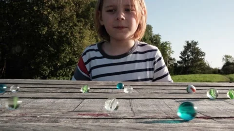 Outdoor fun: a young, long-haired boy enjoying a game with glass marbles on.. Stock Footage 258794355