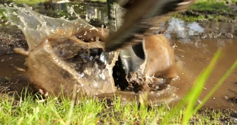 An outdoor man steps into a muddy puddle and makes mud splashing Stock Footage 196136523