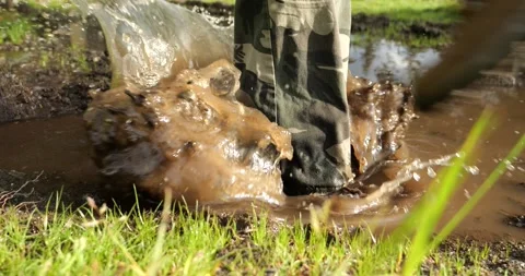An outdoor man steps into a muddy puddle and makes mud splashing Stock Footage 196136549