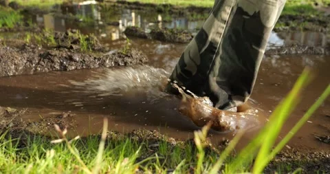 An outdoor man steps into a muddy puddle and makes mud splashing Stock Footage 196136551