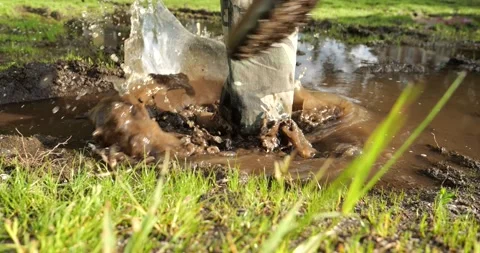 An outdoor man steps into a muddy puddle and makes mud splashing Stock Footage 196136553