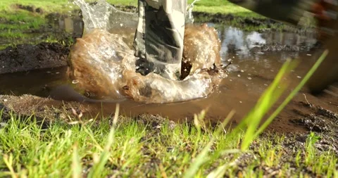 An outdoor man steps into a muddy puddle and makes mud splashing Stock Footage 196136555