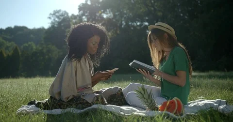 Outdoor picnic on the meadows of two charming mixed race girls. The smiling afro Stock Footage 84519823