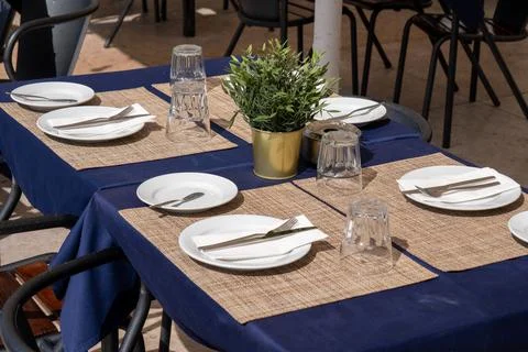 Outdoor Restaurant Table Setting with Blue Tablecloth and Green Plant. Stock Photos