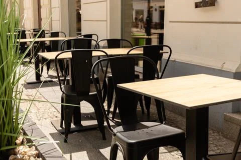An outdoor seating area shows empty tables and chairs arranged next to a bu.. Stock Photos