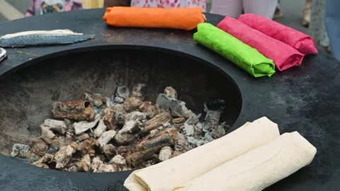 In an outdoor space, individuals prepare flatbreads filled with colorful Stock Footage 345883181