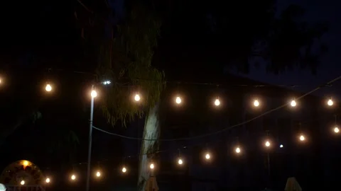 Outdoor string lights glowing at night close up, warm light bulbs garland Stock Footage 342837961