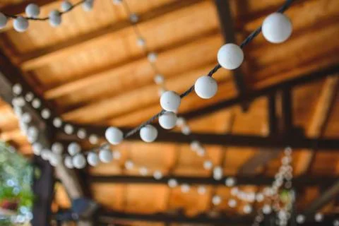 Outdoor string lights hanging on a line with under a wooden roof. Stock Photos