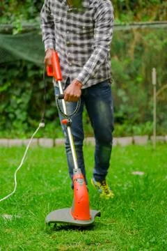 Outdoor view of young worker using a lawn trimmer mower cutting grass in a Fotos de archivo