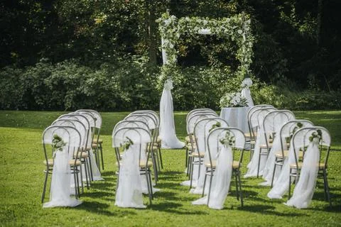 Outdoor wedding ceremony setup featuring white chairs adorned with fabric a.. Stock Photos