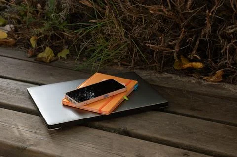 Outdoor Workspace Setup With Laptop, Notebook, and Smartphone On Wooden Bench Foto stock
