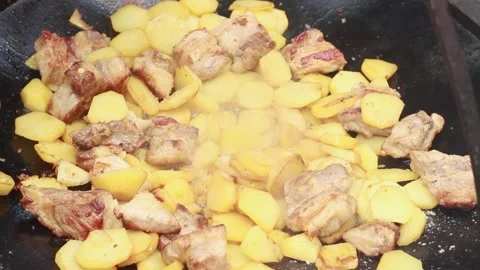 Outdoors we fry tasty potatoes with meat on a bonfire in a giant frying pan on a Stock Footage 136569953