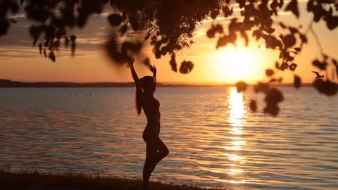 Outlines of a woman meditating by the lake at sunset. A sense of calm and peace. Stock Footage