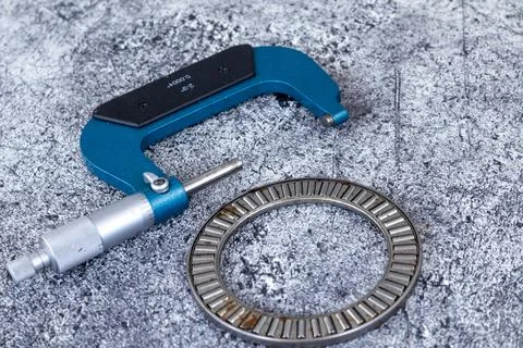 Outside micrometer caliper lying beside needle roller thrust bearing on tex.. Stock Photos