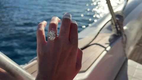 Oval diamond engagement ring glowing in Mediterranean sun on luxury boat deck Stock Footage 319406914