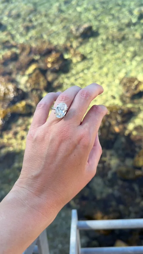 Oval diamond engagement ring held above green crystal clear sea in Croatia Stock Footage 319693639