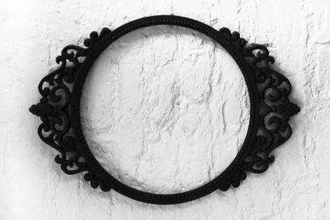An oval patterned empty metal frame on a white wall background. black and whi Stock Photos