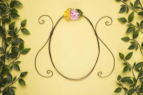 Oval shape frame with artificial rose yellow wall with green leaves 스톡 사진