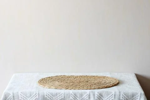 Oval straw mat centered on a white lace tablecloth with a beige wall backgr.. Stock Photos