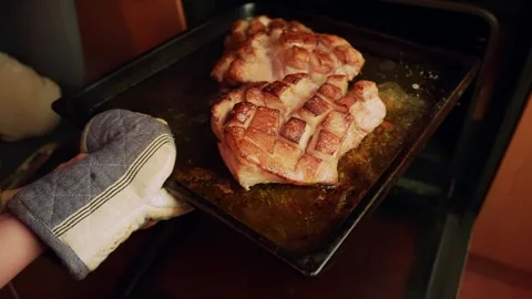 Oven mitt pulls a hot baking tray from the oven, revealing crispy pork belly Stock Footage 328392400