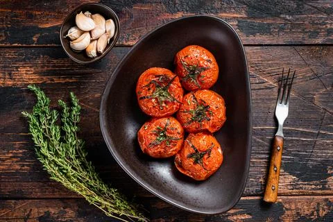 Oven Roasted cherry tomatoes with thyme and garlic in a plate. Dark wooden Stock Photos
