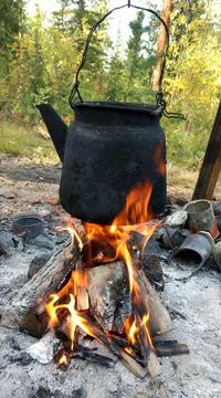 Over the fire hangs an old camp kettle, black with soot and burning. teapot Stock Photos