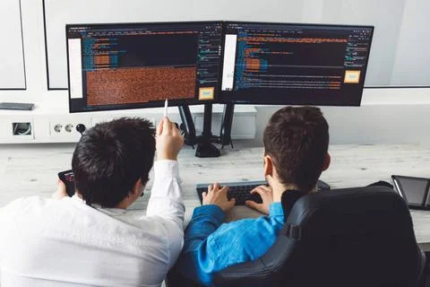 Over the head view, two IT gus working on two screens in the office sittin... Foto stock