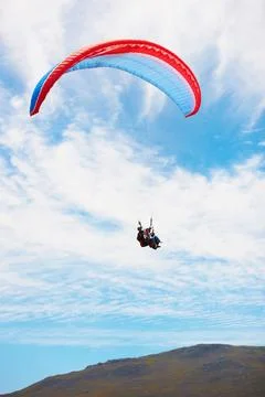 Over the hills...Low angle view of two people doing tandem paragliding high up Stock Photos