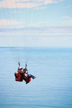 Over the ocean. Side view of two young people doing tandem paragliding with the Stock Photos