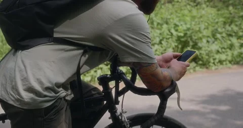 Over-the-shoulder closeup of man using phone on bike in forest Stock Footage 311934554