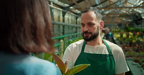 Over the shoulder a confident man with a beard in a green apron talks to a girl Stock Footage 280683874