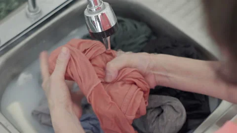 Over the Shoulder Handheld Washing Cothes in Sink Stock Footage 220025593