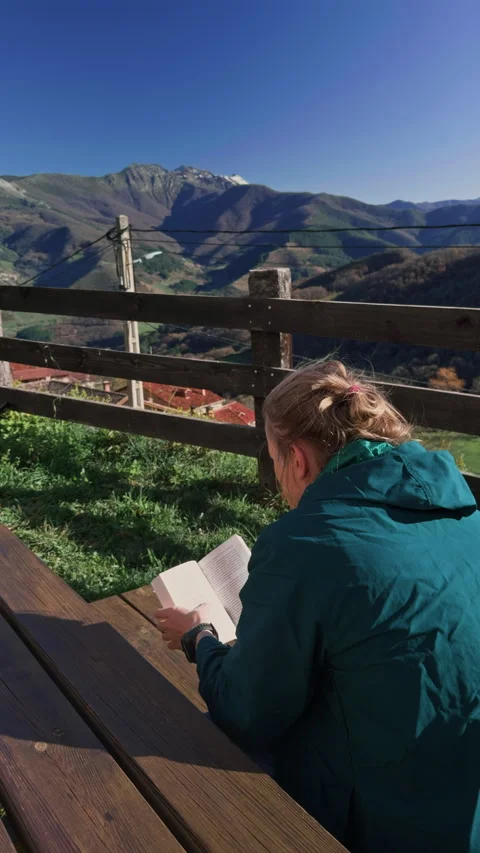 Over shoulder man reading book with mountain view lifestyle 動画素材 332787654
