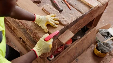 Over-the-shoulder shot of African carpenter sawing wooden plank in workshop  Stock Footage 346733713