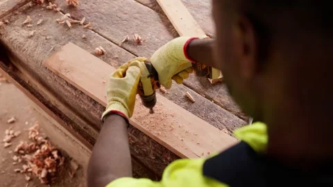 Over-the-shoulder shot of African carpenter drilling wooden plank in shop Stock Footage 346733786