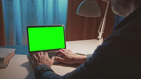 Over the shoulder shot of bearded unrecognazable man typing on laptop with green Stock Footage 148480567