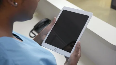 Over the shoulder shot of an iPad or tablet held by a nurse in blue scrubs Stock Footage 109503827