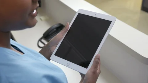 Over the shoulder shot of  iPad or tablet held by a nurse in blue scrubs talking Stock Footage 109503828