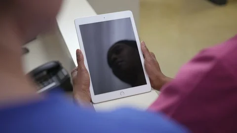 Over the shoulder shot of  iPad, tablet framed by shoulders of two female nurses Stock Footage 109504004