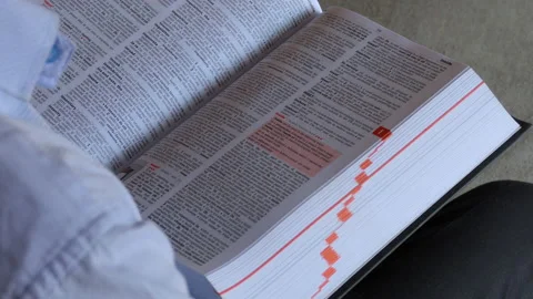 Over the shoulder shot of a man sitting on a chair and reading a dictionary Stock Footage 147007183