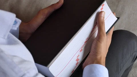 Over the shoulder shot of a man sitting on a chair and holding a thick book Stock Footage 147010255