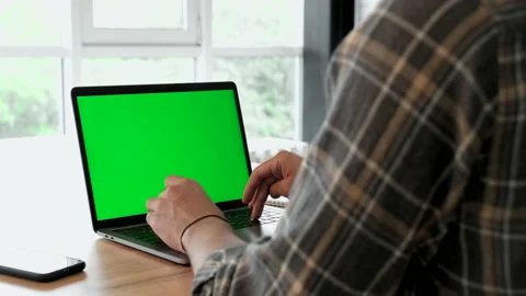 Over the shoulder shot of a man typing on a computer laptop with green screen Stock Footage 186944632