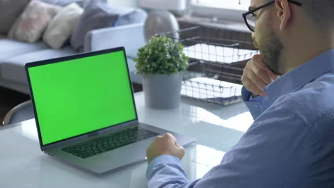 Over the shoulder shot of man working on laptop with green screen display Stock Footage 146319382