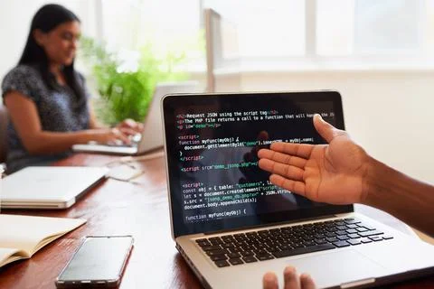 Over the shoulder shot of young developer gesture to code on laptop in office Stock Photos