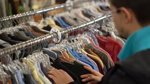 Over the shoulder shot of young man looking through shirts on a rack. Stock Footage 99310765