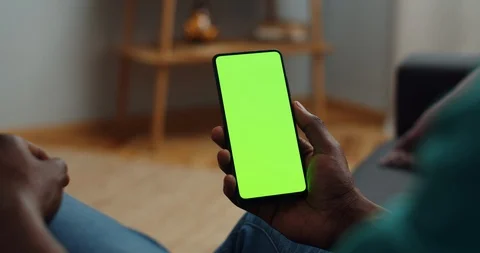 Over shoulder view of afro american man sitting on couch and holding smartphone Video stock 128574266