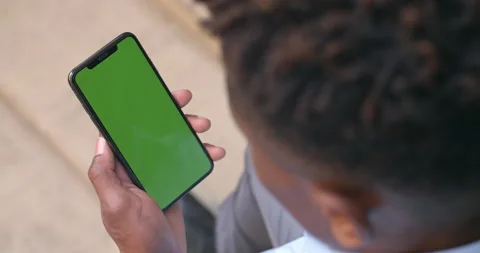 Over shoulder view of afro american guy sitting and looking at phone green Stock Footage 130233155