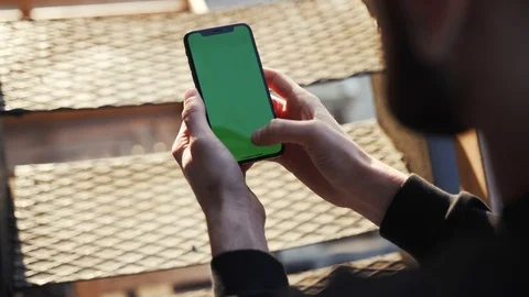 Over shoulder view of bearded man using smartphone with green screen, tapping Stock Footage 104906376