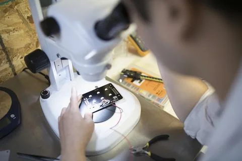 Over the shoulder view engineer examining electronics with microscope Stock Photos