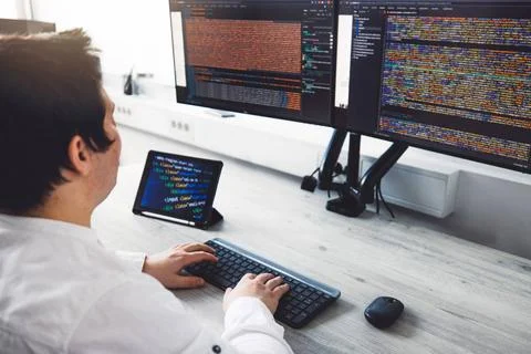 Over the shoulder view IT guy working on two screens coding on desktop com... Stock-Fotos